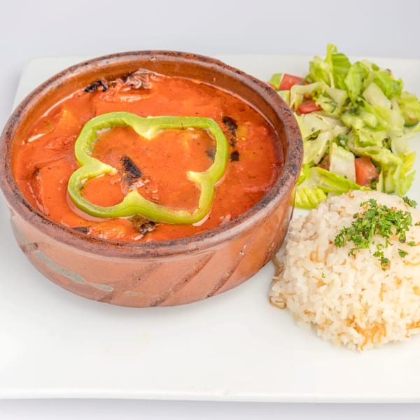 A middle-eastern dish in a clay pot with tomato sauce, green bell pepper, rice, and salad.