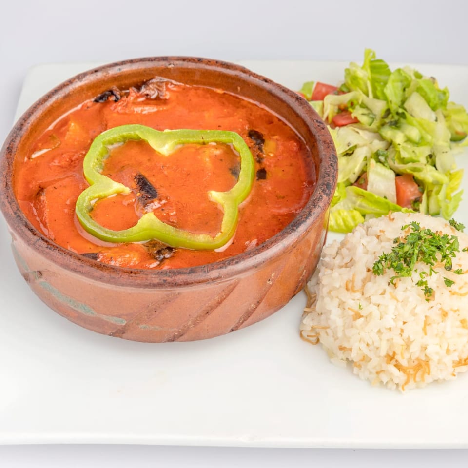 A middle-eastern dish in a clay pot with tomato sauce, green bell pepper, rice, and salad.