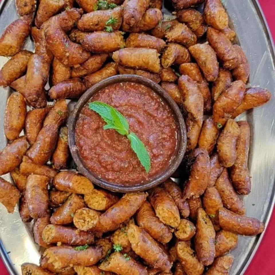 A platter of golden-brown Egyptian mombar, rice-stuffed sausages, with a bowl of red dipping sauce and mint.