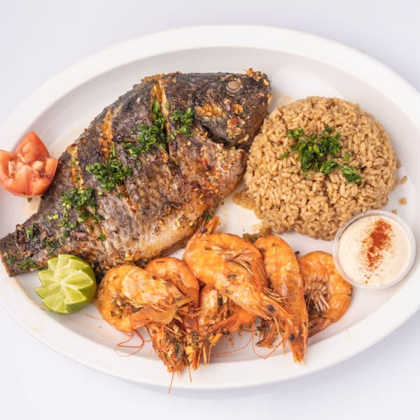 Grilled whole fish, shrimp, rice, lime, tomato, and sauce on a white plate.