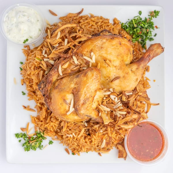 Whole roasted chicken on a bed of rice with fried onions, almonds, parsley, and two dipping sauces.