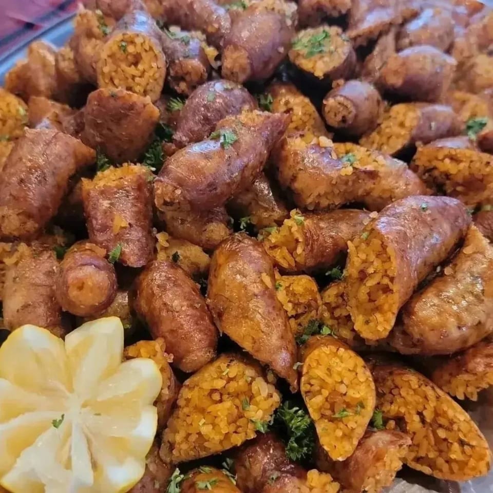 A platter of golden-brown Egyptian mombar, rice-stuffed sausage, garnished with parsley and a lemon slice.