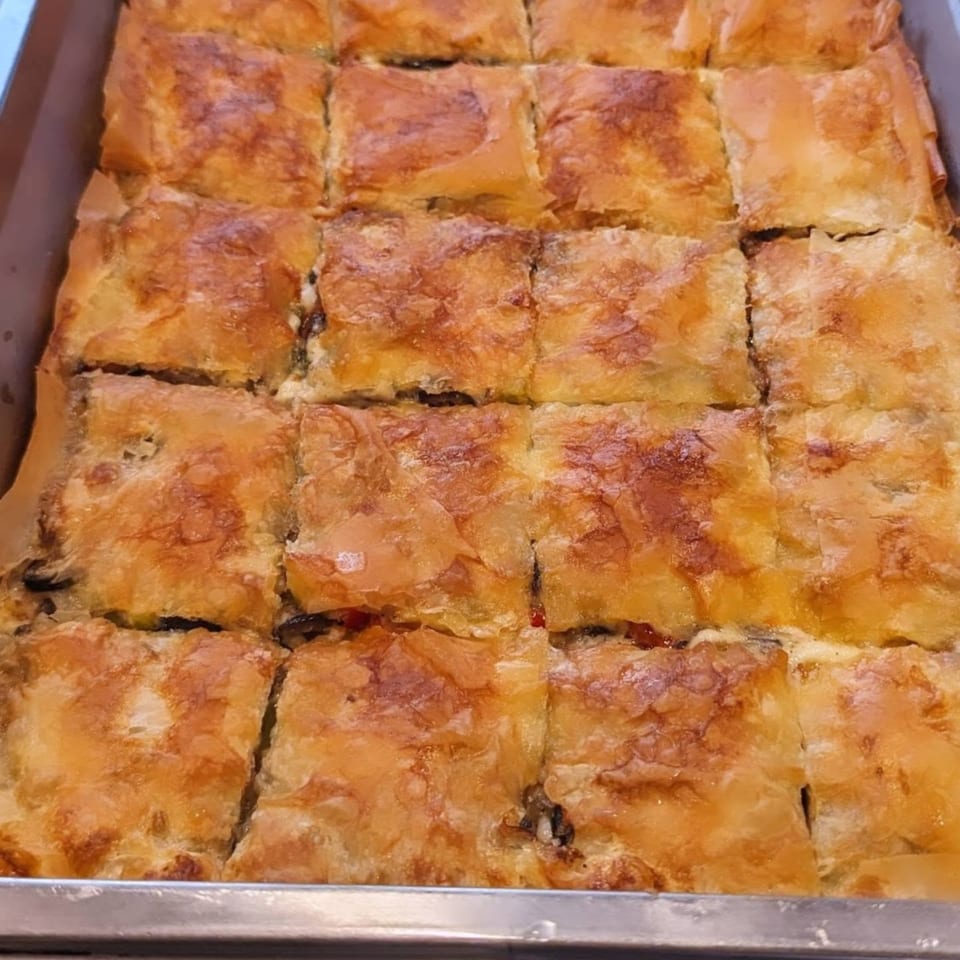 Close-up of a tray of golden-brown, square-cut Middle Eastern pastries, possibly baklava or bourekas.