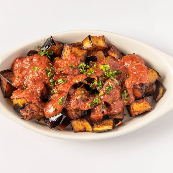 Roasted eggplant cubes topped with a rich red sauce and fresh green herbs in a white dish.